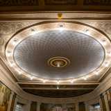 Al di sotto di un soffitto riccamente decorato con motivi vegetali grigi e dorati...